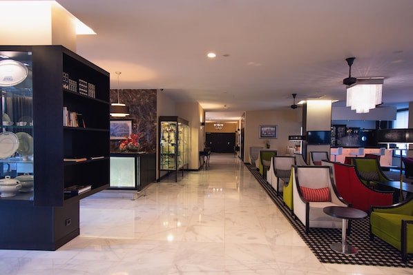 A modern hotel lobby with a marble floor, a black bookshelf, a glass display case, and colorful seating areas. - SANA Silver Coast Hotel (Caldas da Rainha)