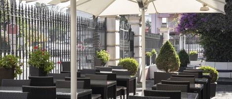 An outdoor seating area with wicker tables and chairs, umbrellas, and potted plants.