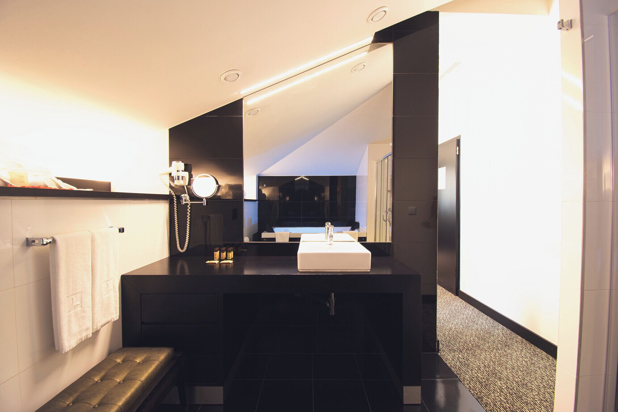 A modern bathroom with a vanity, a mirror, and a bench.