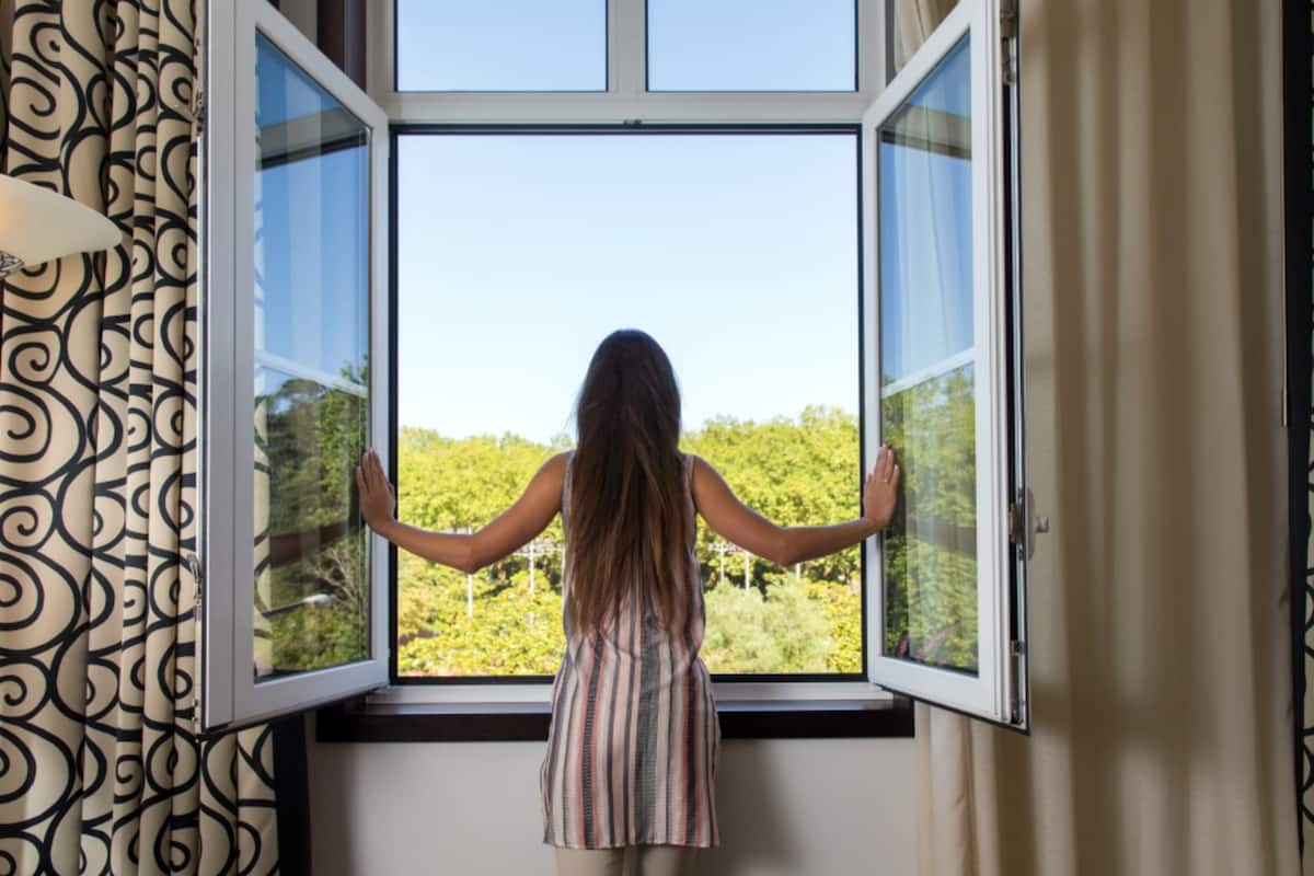 A person standing by an open window with a view of greenery outside.