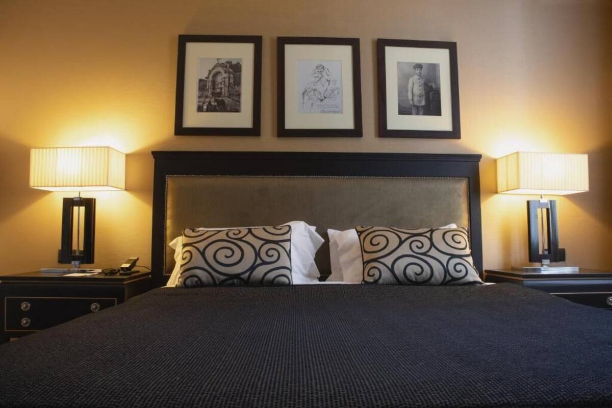 A hotel room with a large bed, two bedside tables, a headboard, and three framed pictures on the wall.