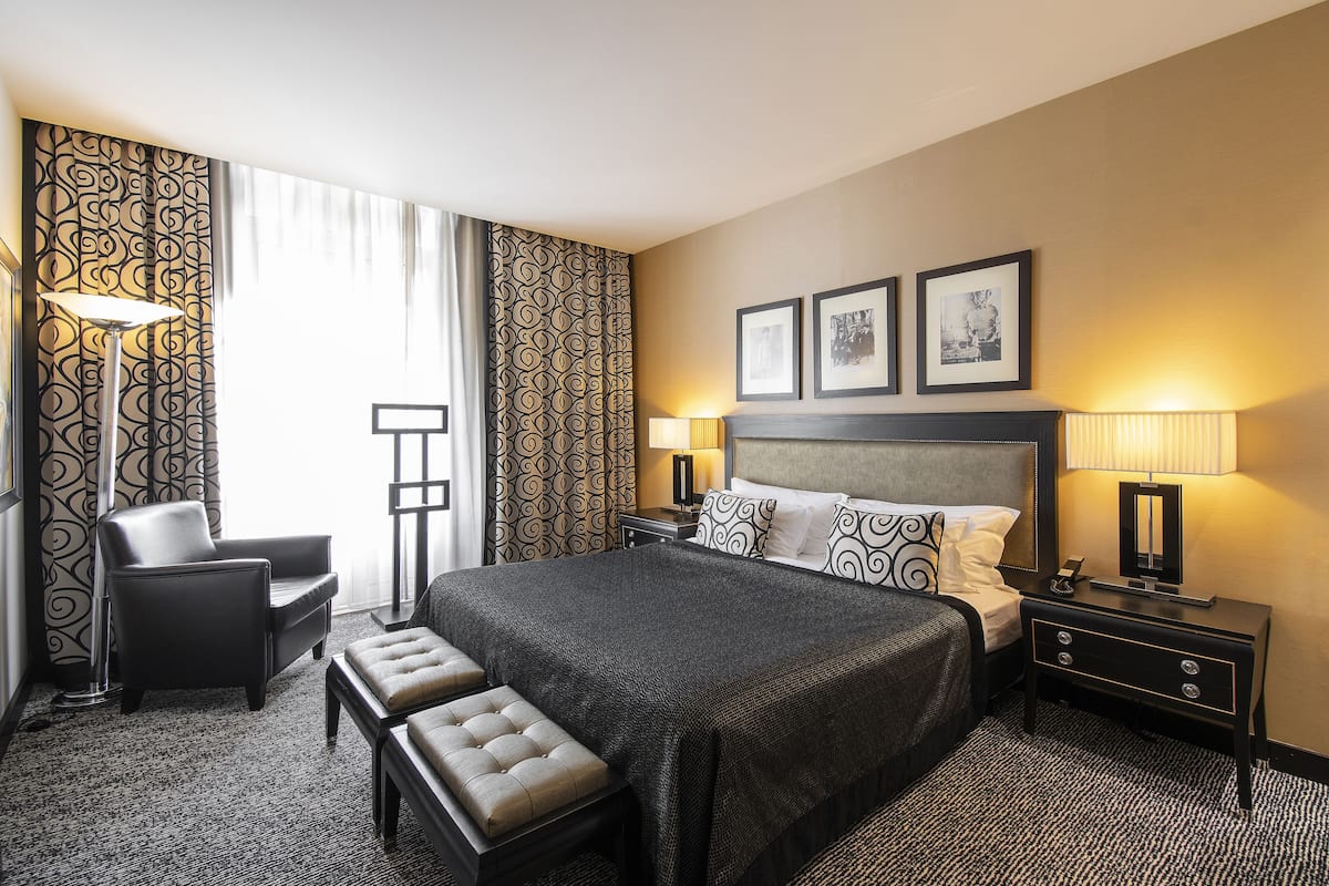 A hotel room with a large bed, a desk, a chair, a bench, and two bedside lamps.