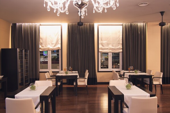 A dining area with tables and chairs, large windows with curtains, and a chandelier. - SANA Silver Coast Hotel (Caldas da Rainha)