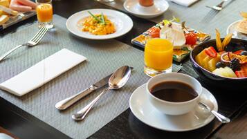 A breakfast table with plates of food, a glass of orange juice, a cup of coffee, and cutlery.