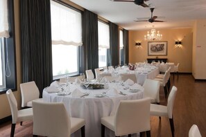Un espace repas avec des tables rondes, des chaises blanches et un lustre.