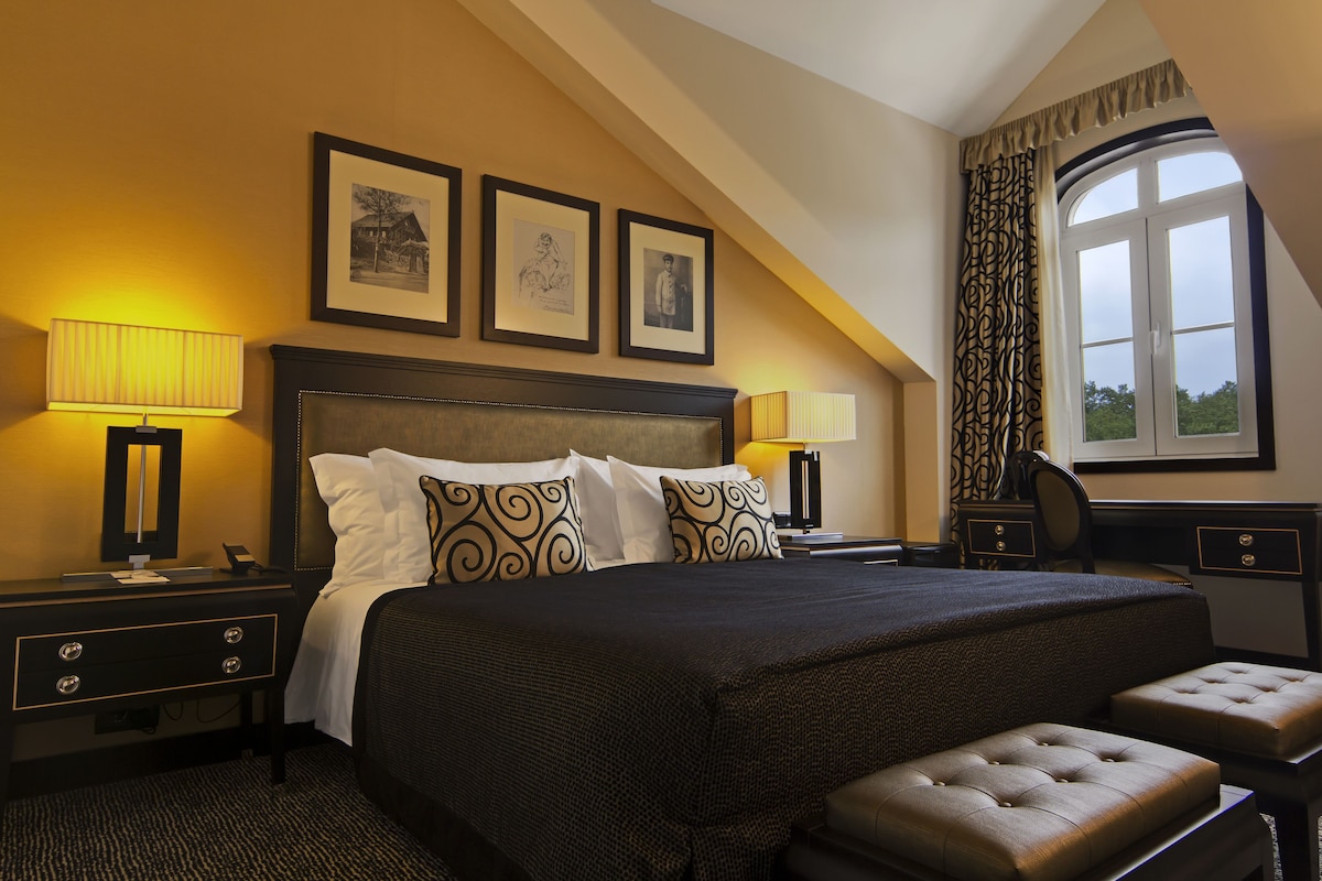 A hotel room with a large bed, two bedside tables, a desk, and a window with curtains.