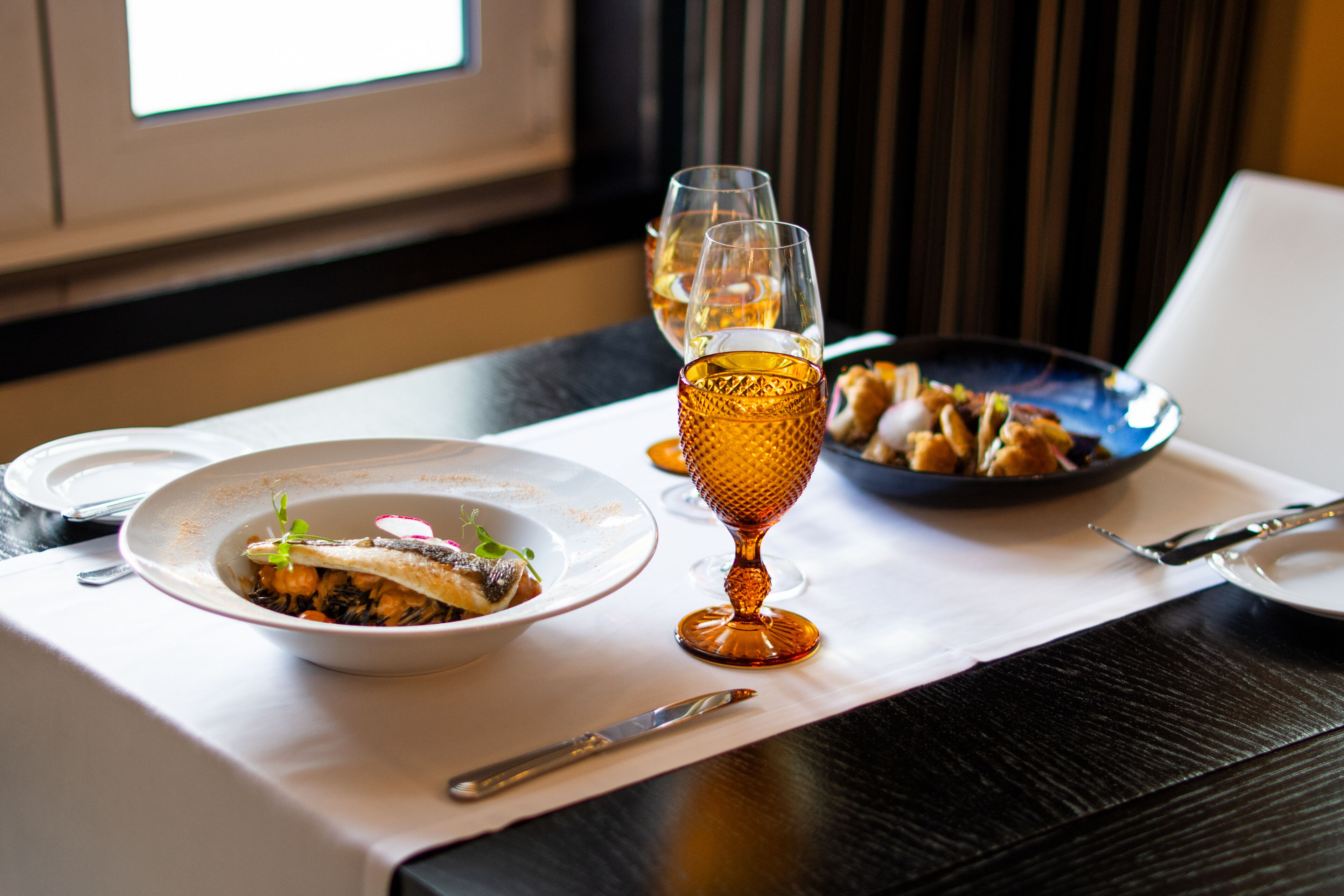 Une table à manger avec une assiette de nourriture, un verre de vin et un bol de noix.