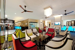 A modern hotel lobby with multiple seating areas, ceiling fans, and a bar area.