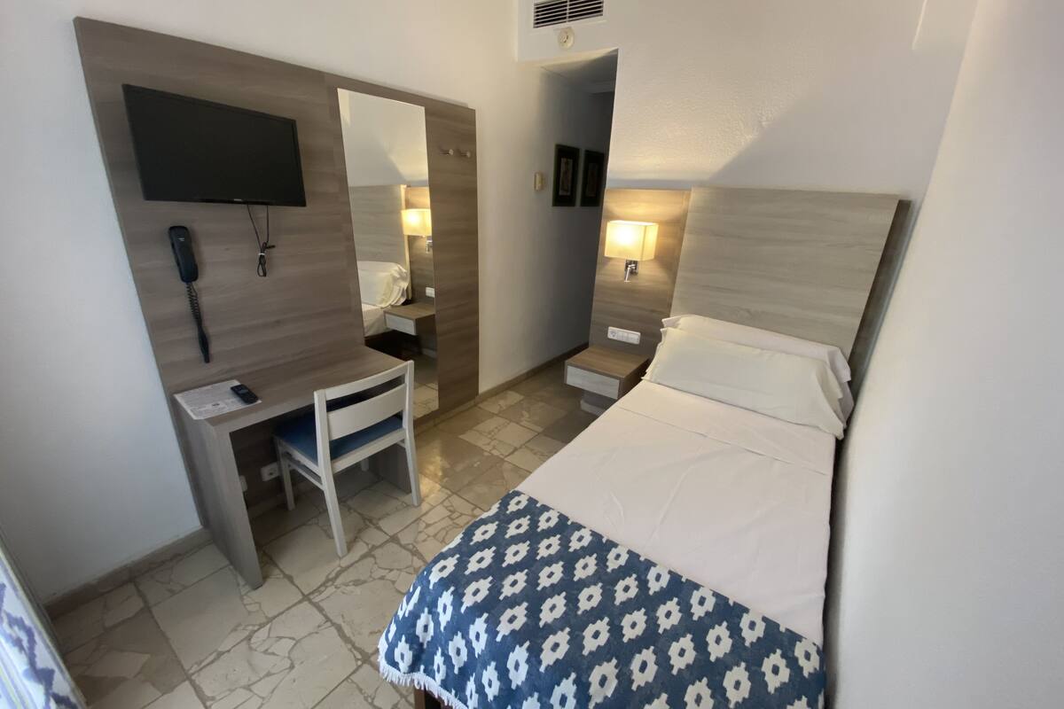 Et hotelværelse med seng, skrivebord, stol og et fjernsyn ophængt på væggen.