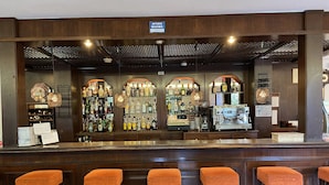 A bar area with wooden bar counters, multiple liquor bottles, a coffee machine, and four orange cushioned stools. - Hostal Villa Rosa (Calvia)