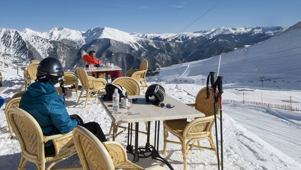 Una mesa con sillas de mimbre con vistas a un paisaje montañoso nevado.