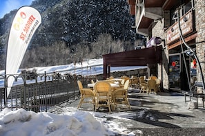 A snow-covered outdoor seating area with wicker chairs and a stone building in the background. - Apartaments Sant Moritz (Arinsal)