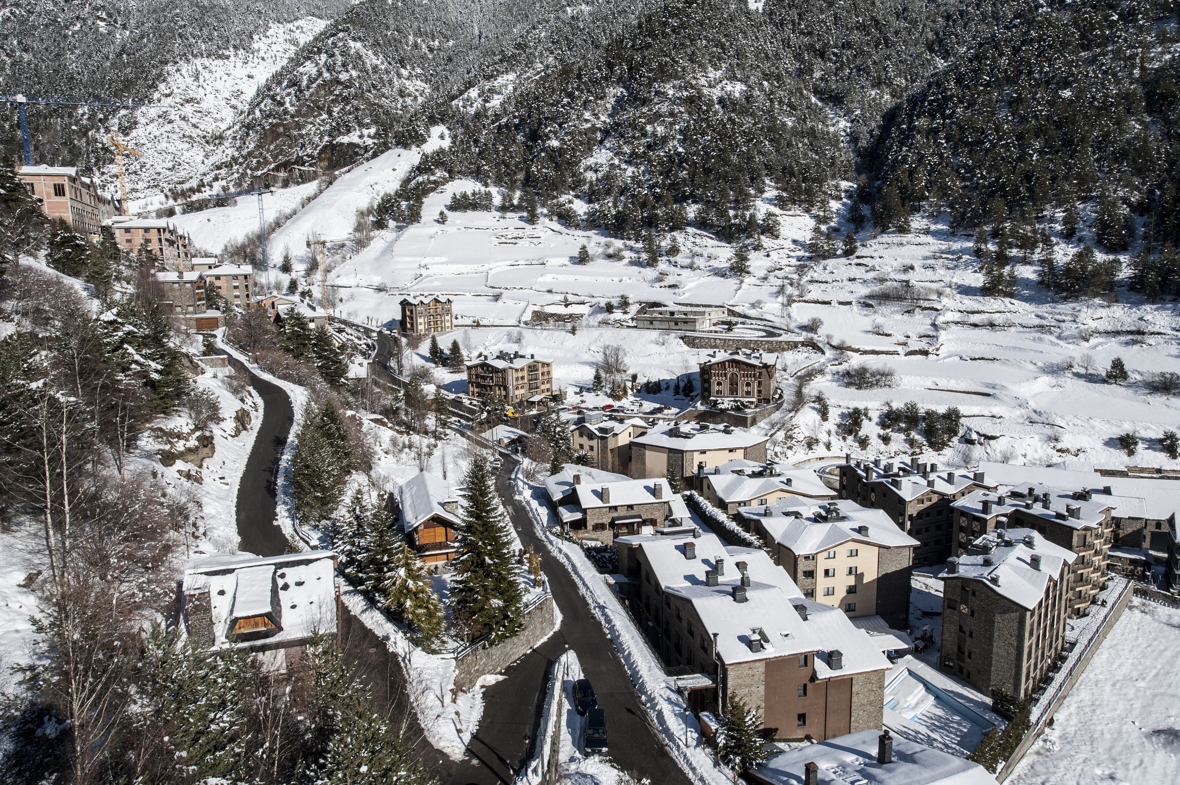 Un pueblo cubierto de nieve con edificios, una carretera sinuosa y una montaña al fondo.