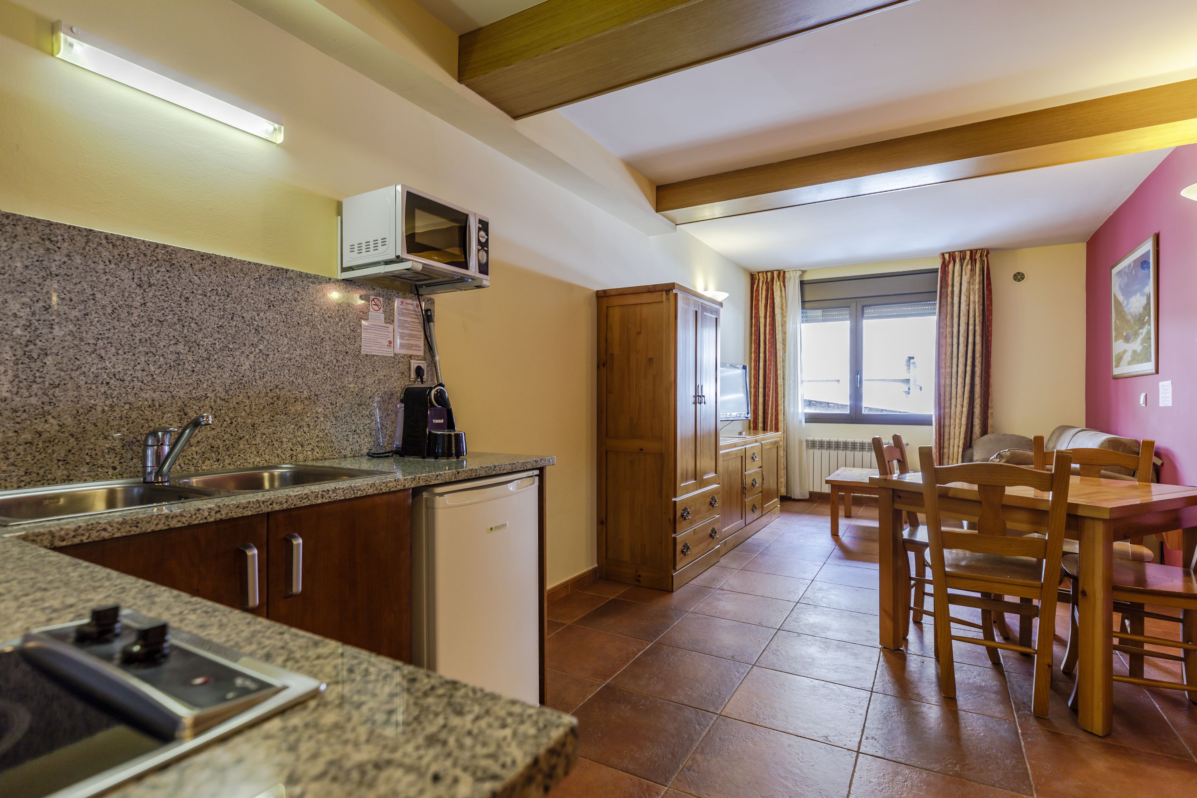 A compact kitchen with granite countertops, a built-in microwave, and a dishwasher. There is a dining area with a wooden table and chairs.