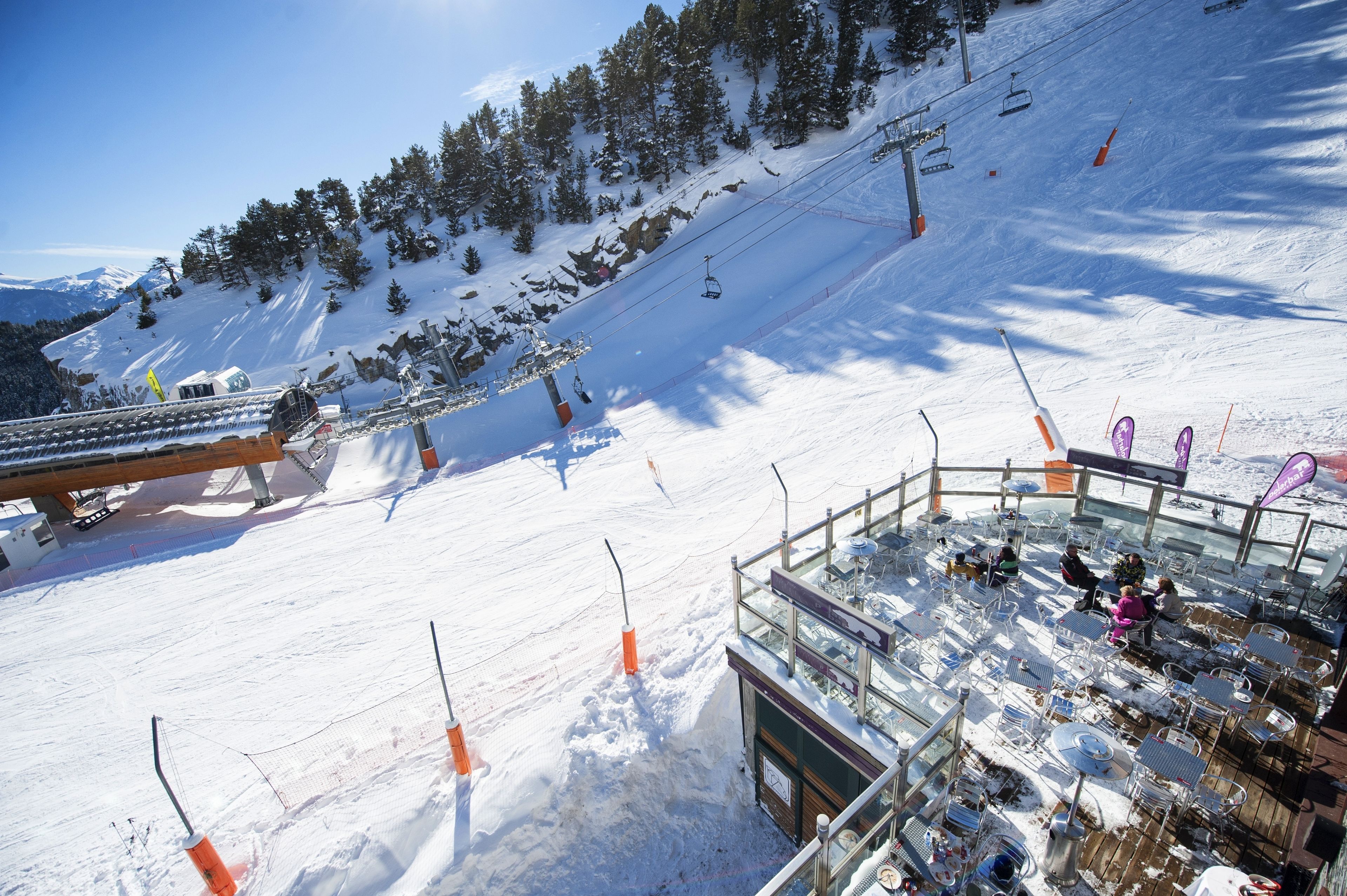 A ski resort with a chairlift, snow-covered slopes, and a glass-enclosed area with tables and chairs.