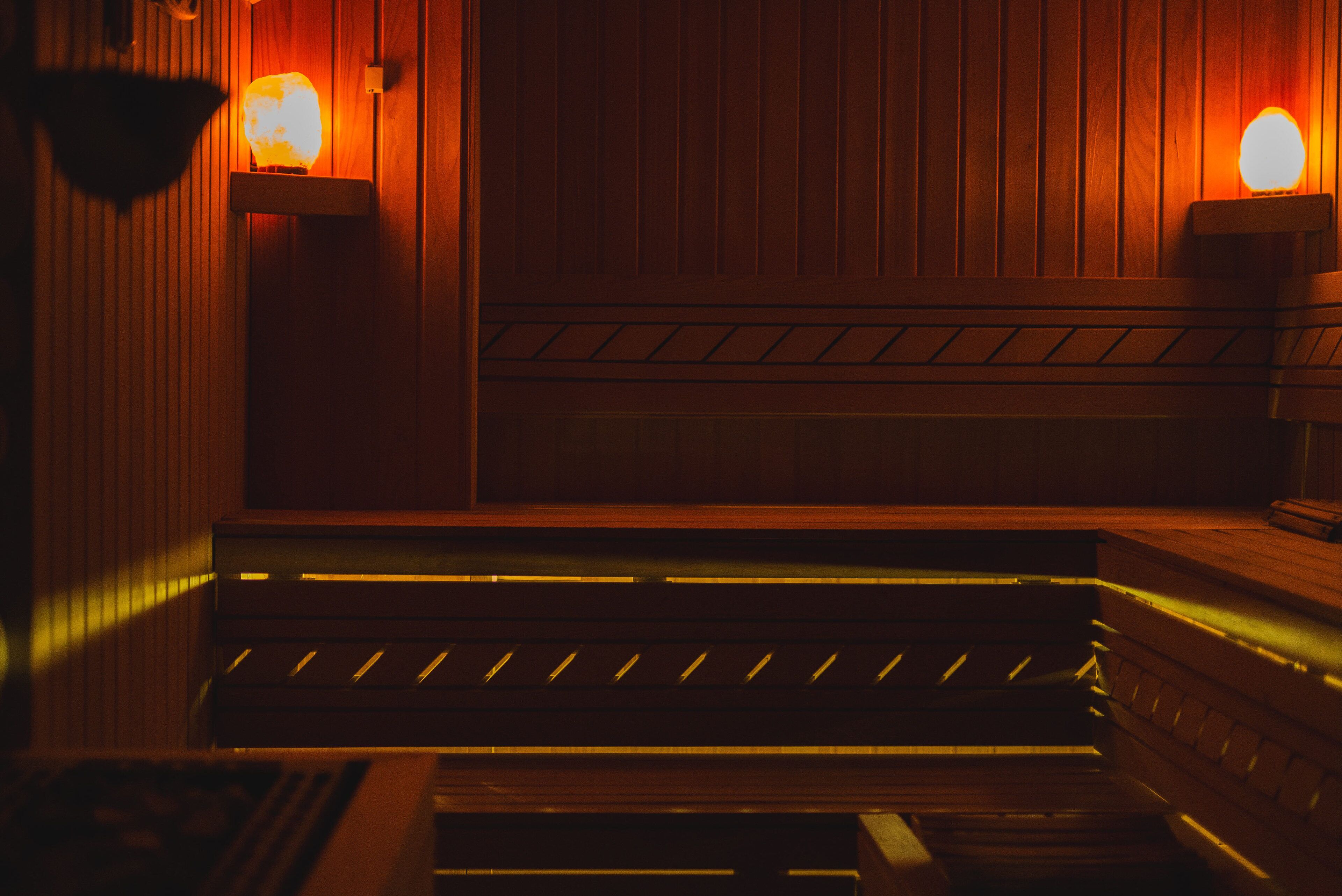 A sauna with wooden walls and benches, and two wall-mounted light fixtures.