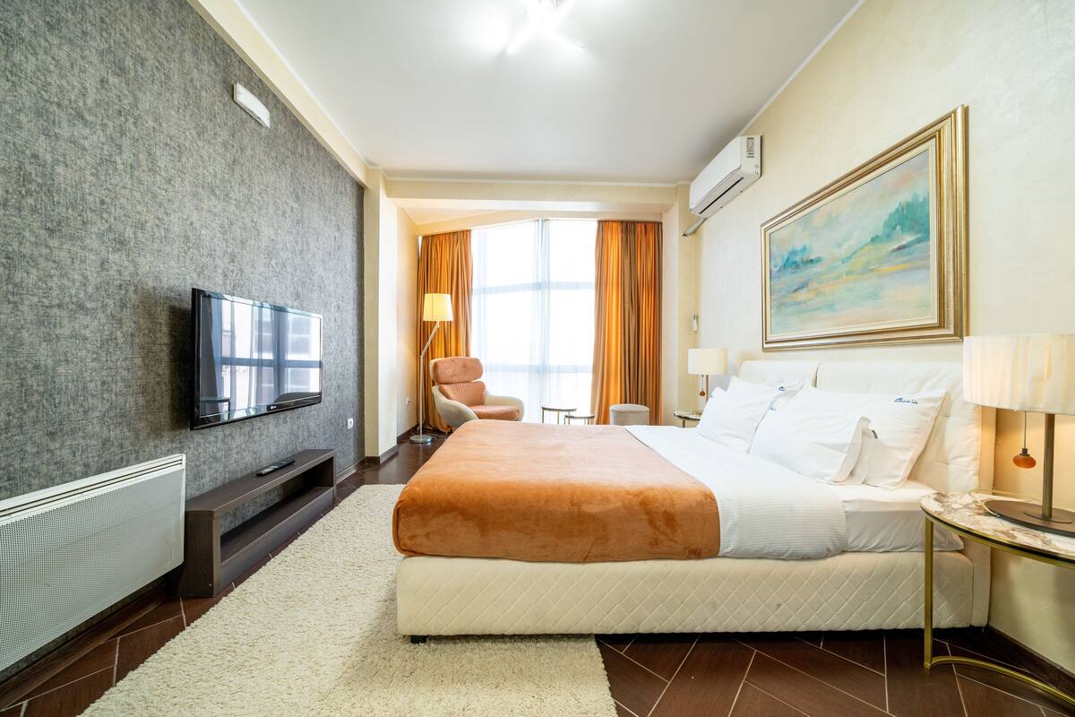 A hotel room with a large bed, a flat-screen TV, a desk with a lamp, and a painting on the wall.