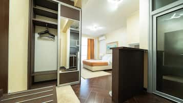 A hotel room with a walk-in closet, a bed, a desk, and a large window.