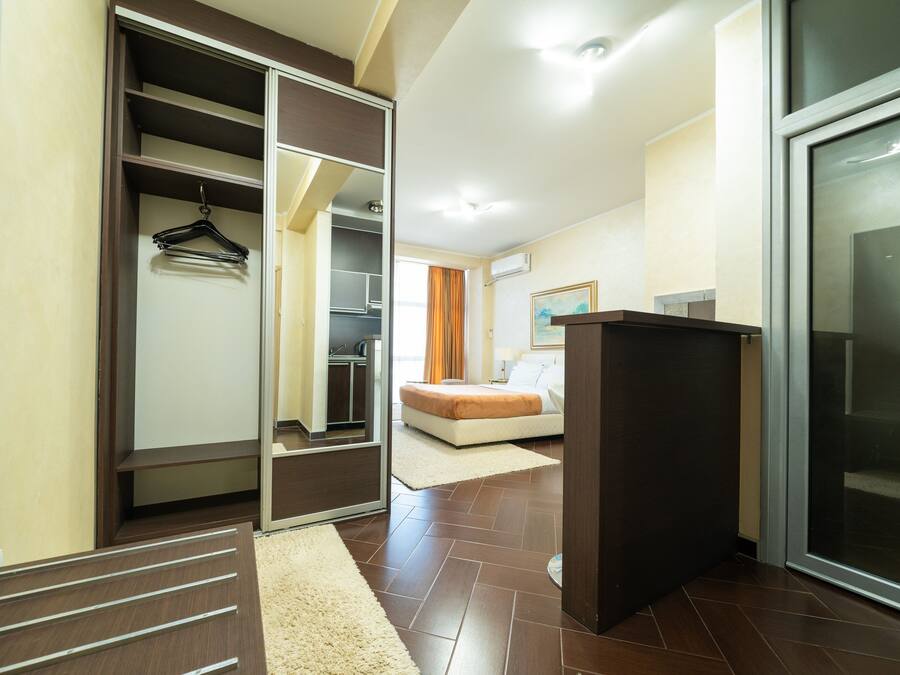 A hotel room with a walk-in closet, a bed, a desk, and a large window.