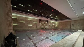 Ein großer, überdachter Schwimmbereich mit Fliesenboden und hoher Decke mit eingelassener Beleuchtung.