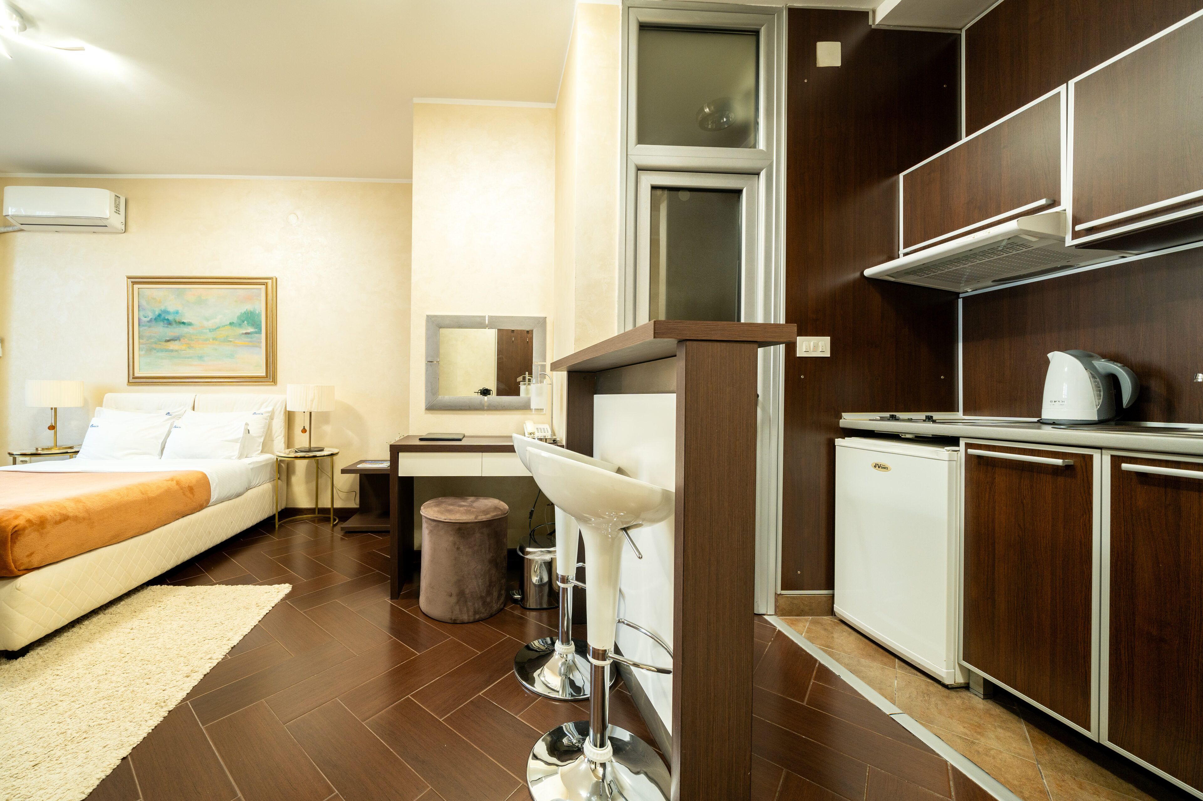 A hotel room with a bed, bedside table, lamp, and a kitchenette with a sink and a small refrigerator.