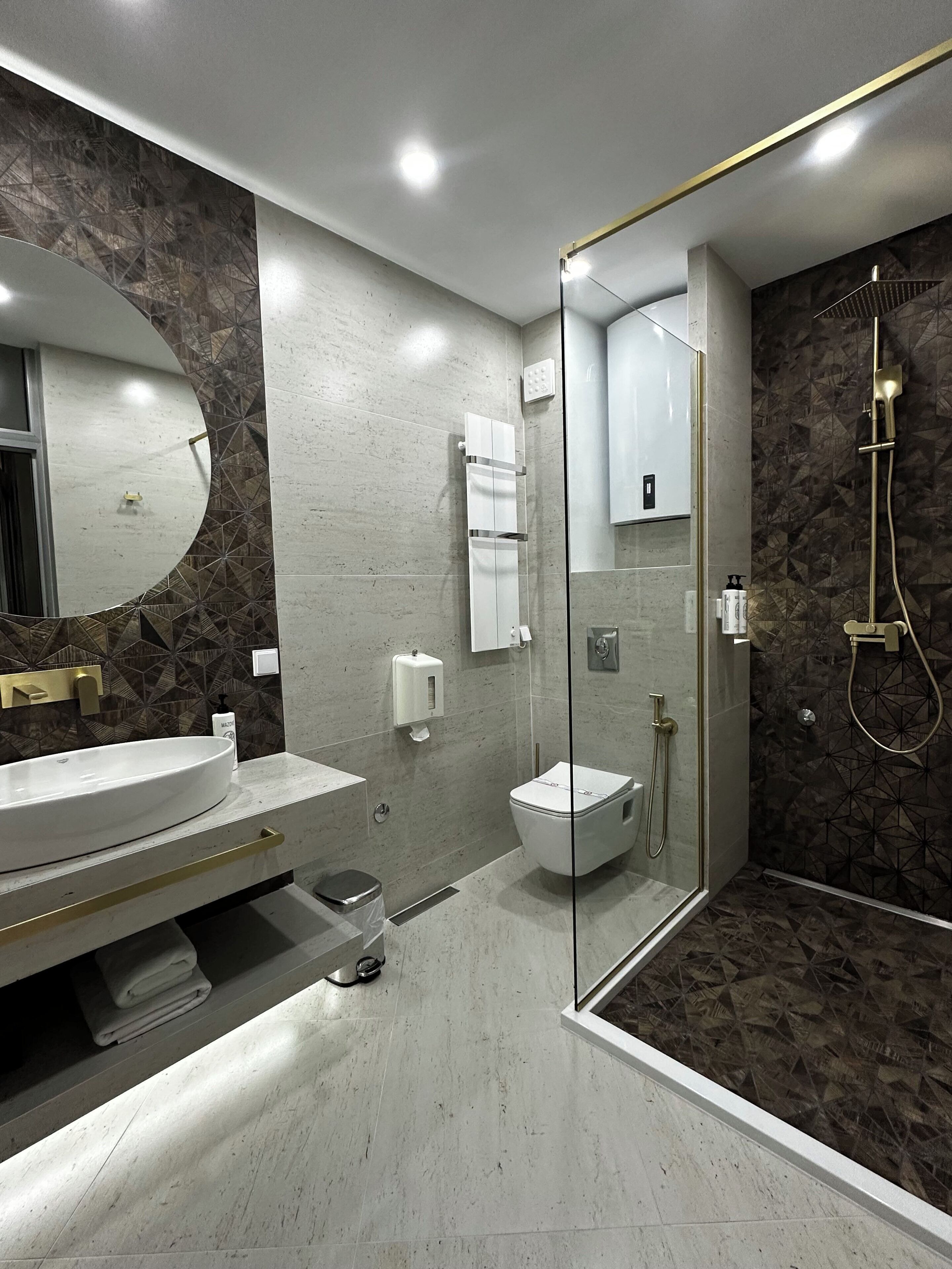 Une salle de bain moderne avec un grand miroir ovale, une douche à parois de verre et des toilettes.