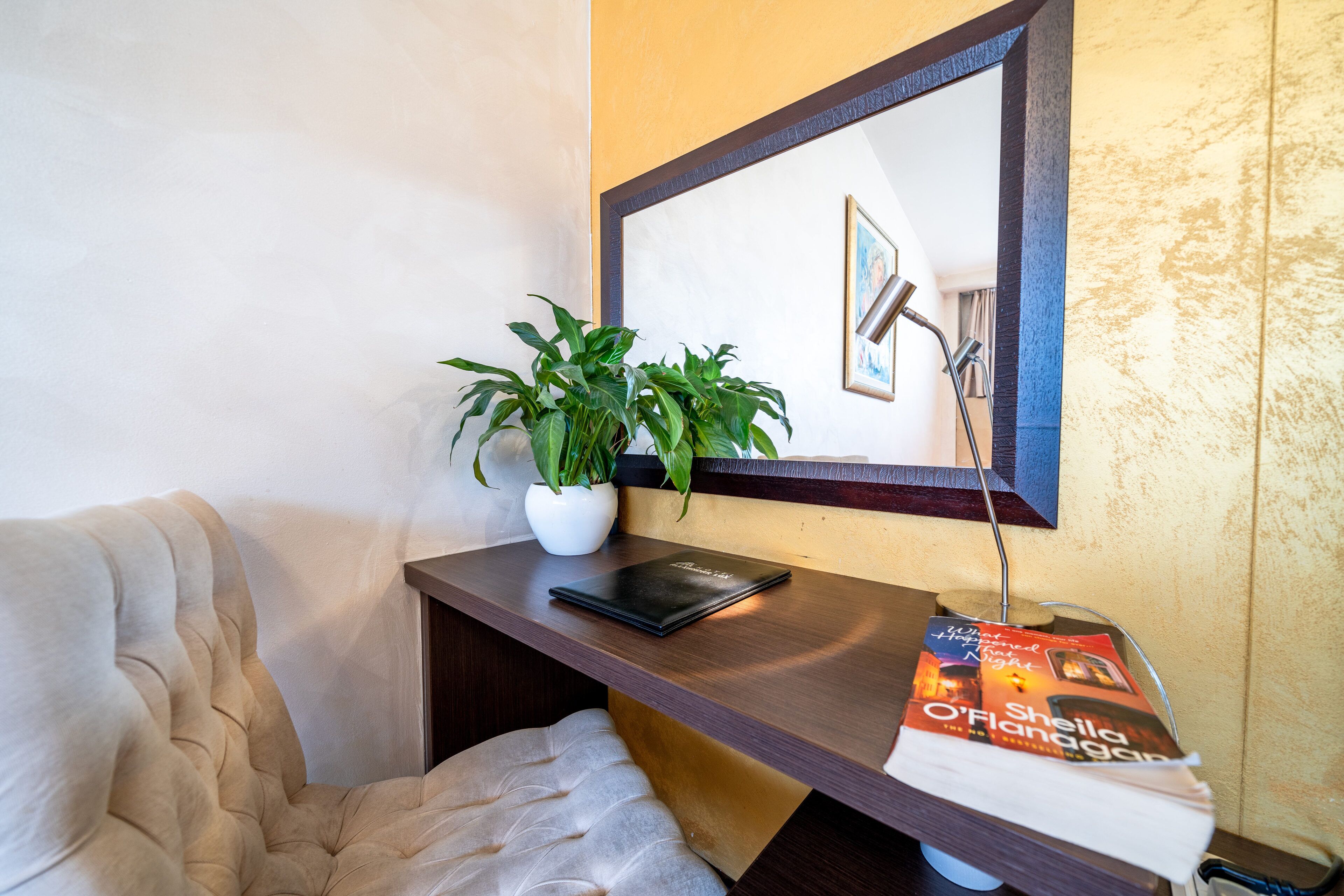 Un coin de pièce avec un fauteuil rembourré, une petite table sur laquelle est posée une plante en pot, un tableau encadré et un magazine.