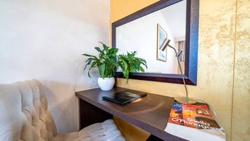 A corner of a room with a cushioned chair, a small table with a potted plant, a framed picture, and a magazine.