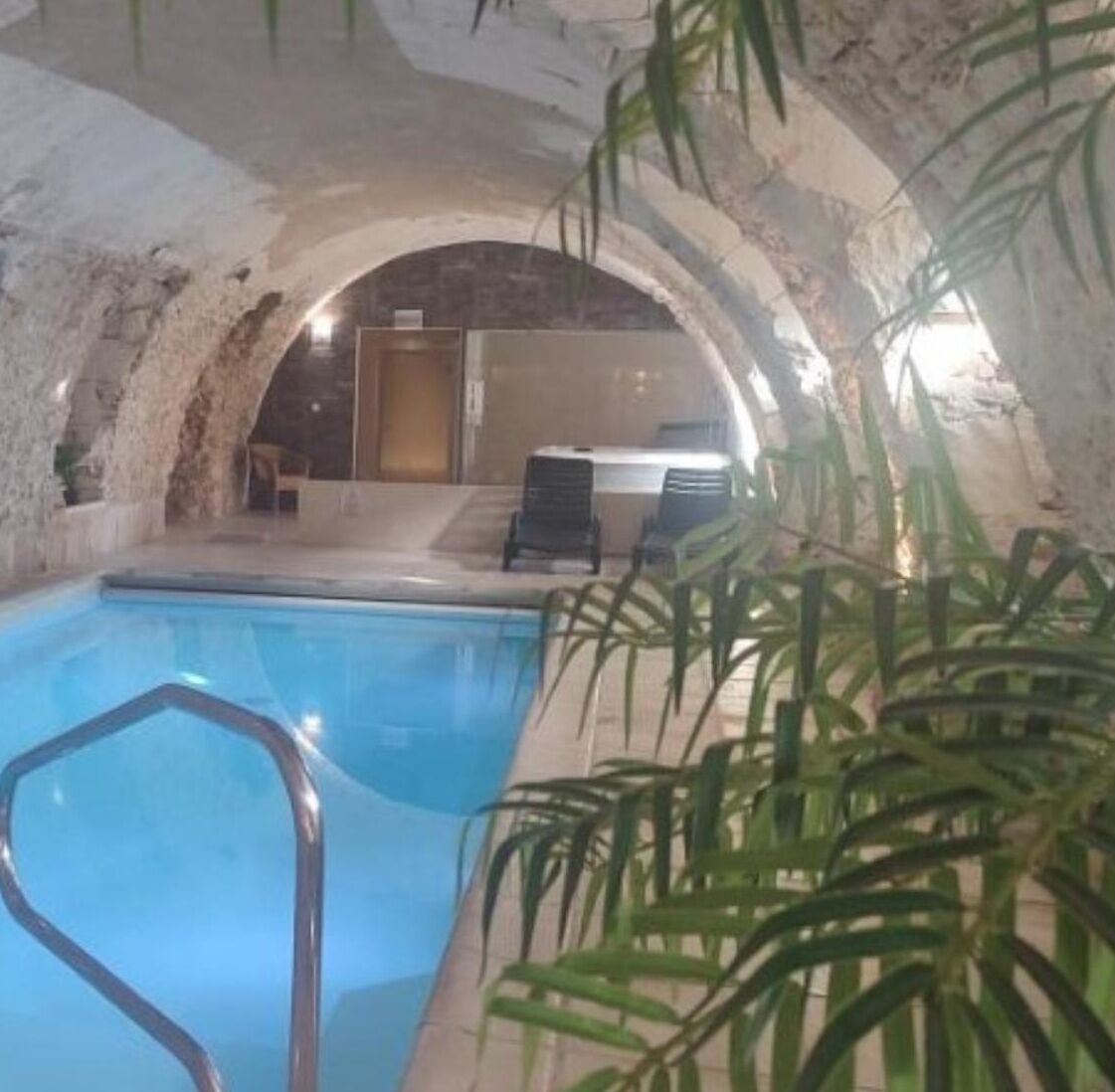 An indoor swimming pool with a stone archway, lounge chairs, and potted plants.