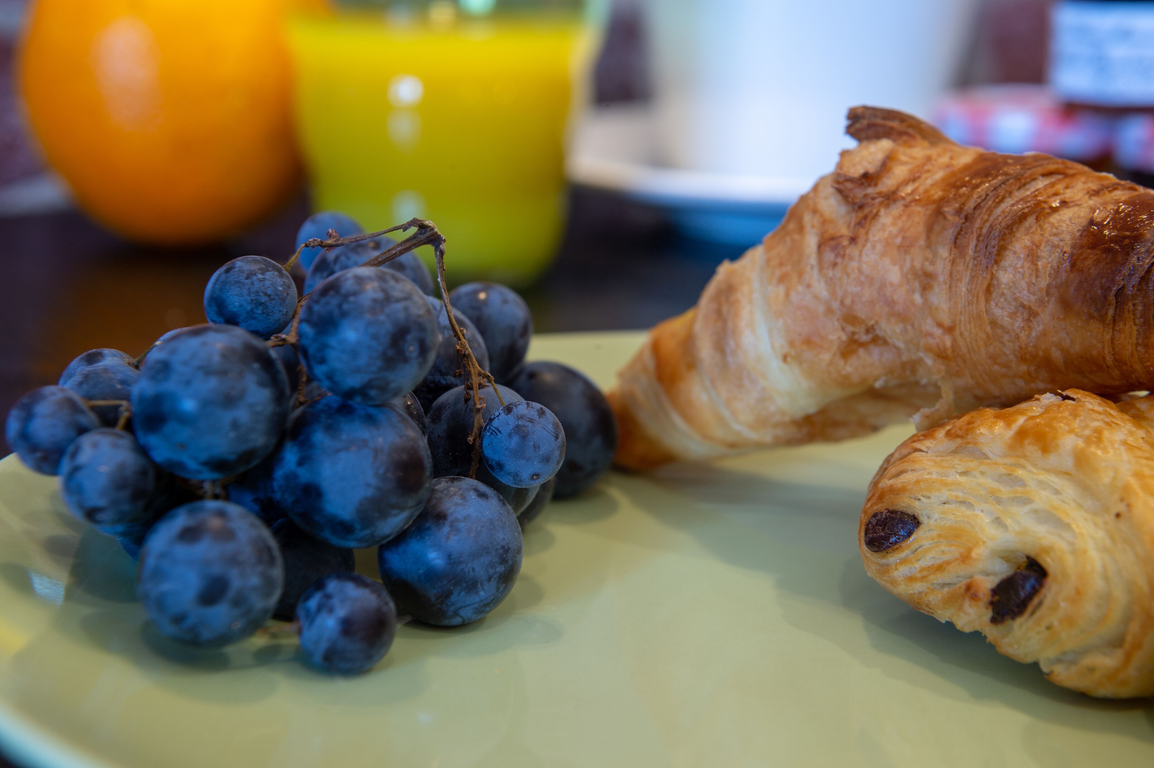 A plate with a croissant and a bunch of grapes.