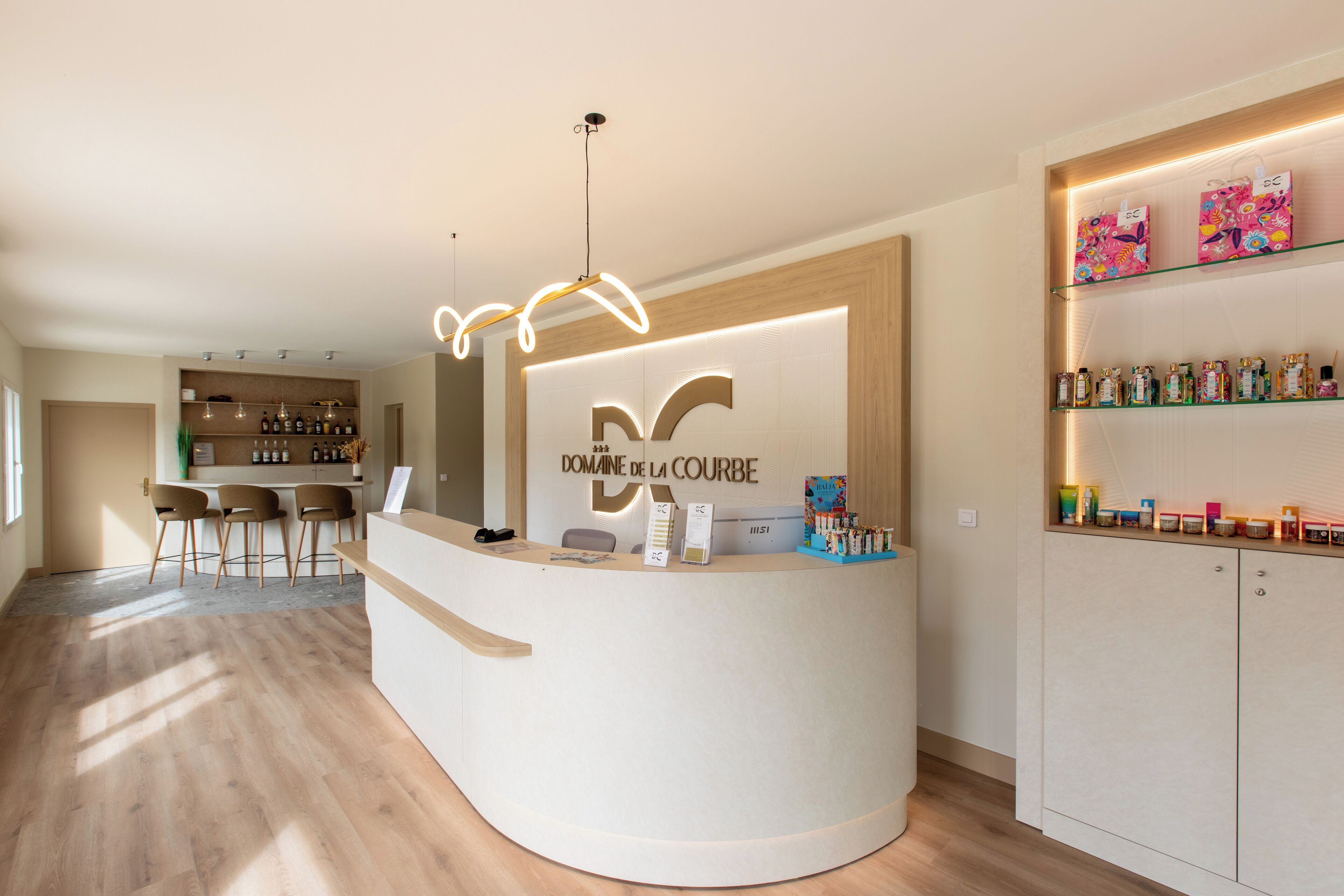 A reception area with a curved counter, a sign reading "DOMAINE DE LA COURBE," and a shelf with various items.