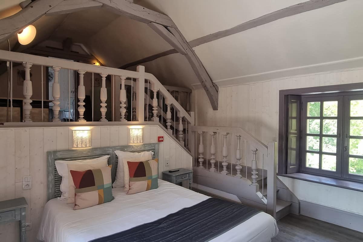 A bedroom with a bed, a nightstand, a dresser, a window, and a staircase with a railing.