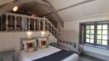 Ein Schlafzimmer mit Bett, Nachttisch, Kommode, Fenster und Treppe mit Geländer.