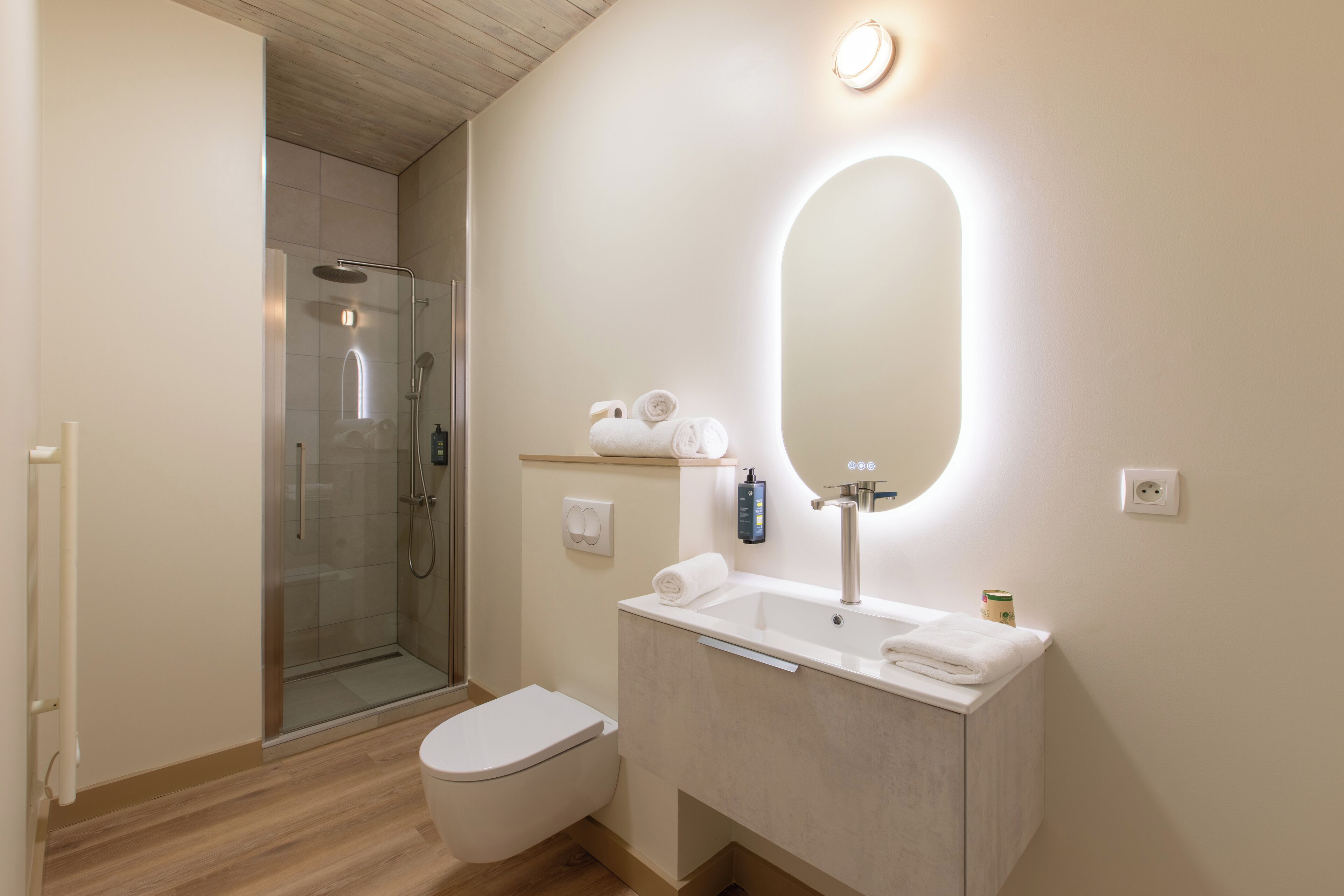 Un baño moderno con ducha de vidrio, inodoro, lavamanos con espejo y dispensador de toallas.
