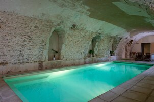 A swimming pool with stone walls and arches, potted plants, and a few chairs.