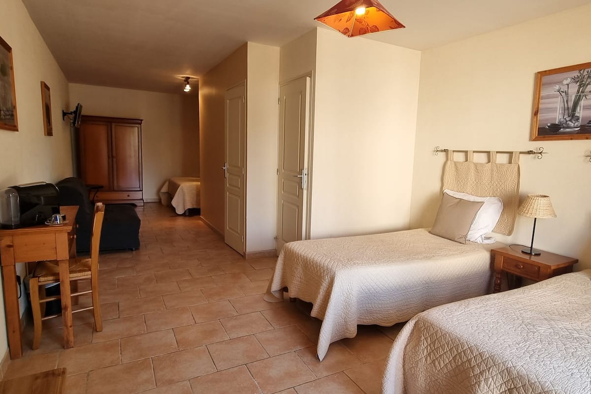 A hotel room with two beds, a desk with a computer, a chair, and a wardrobe.