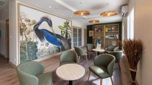 A modern interior with green upholstered chairs, a round wooden table, and a large mural of a bird.