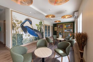 A modern interior with green upholstered chairs, a round wooden table, and a large mural of a bird.