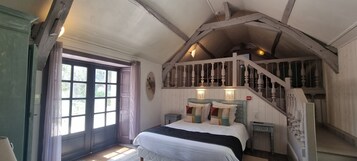 A bedroom with a large bed, a staircase, and a window with curtains.