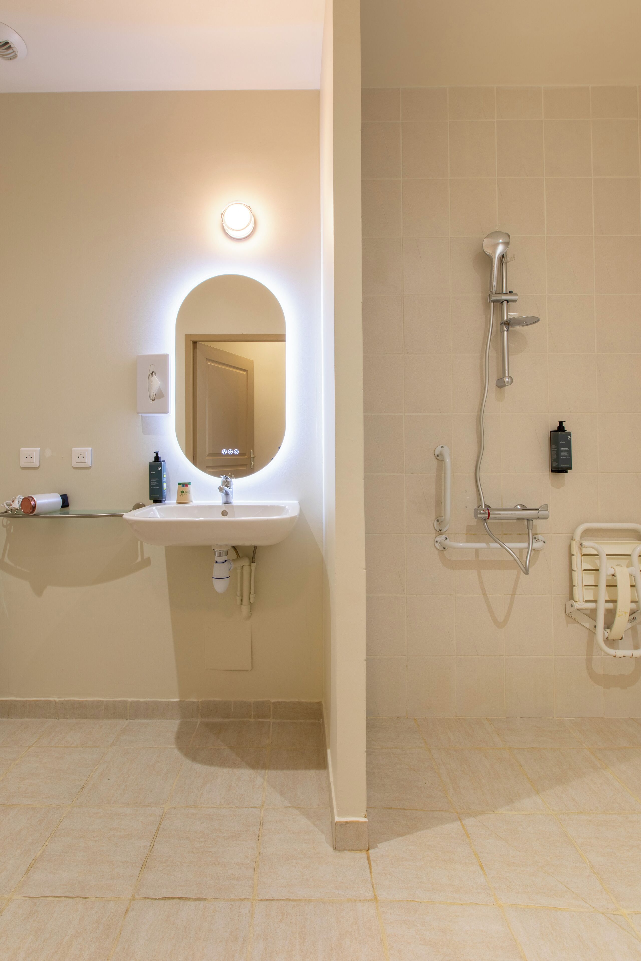 Un baño con lavamanos, espejo, ducha y barras de apoyo.