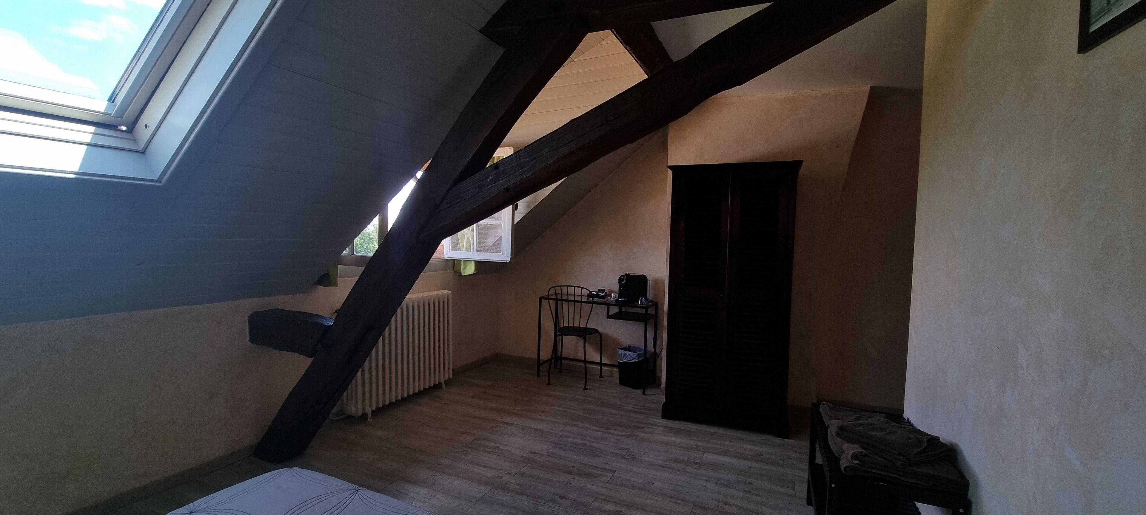 A sloped ceiling room with a skylight, a radiator, a chair, and a door.