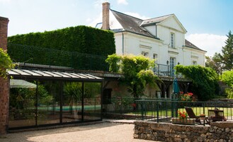 A covered outdoor area with a glass enclosure, a stone wall, and a white building with a green roof in the background.