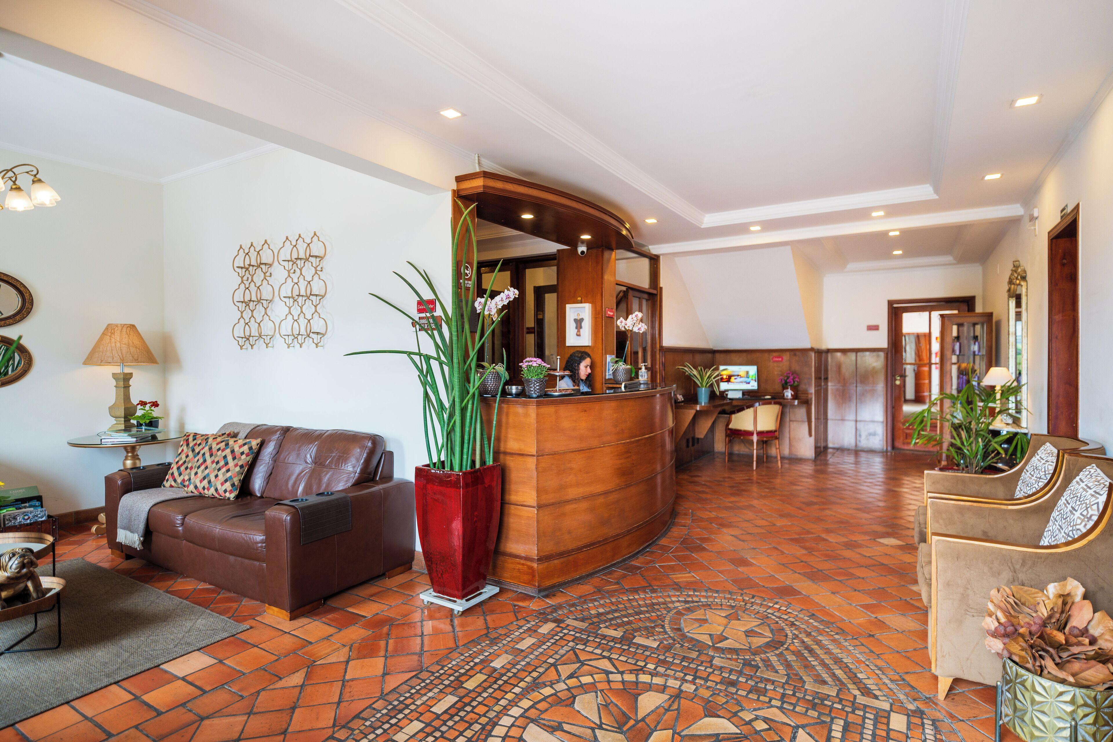 Um hall amplo com balcão de recepção, sofás de couro, um tapete estampado e piso em azulejo.
