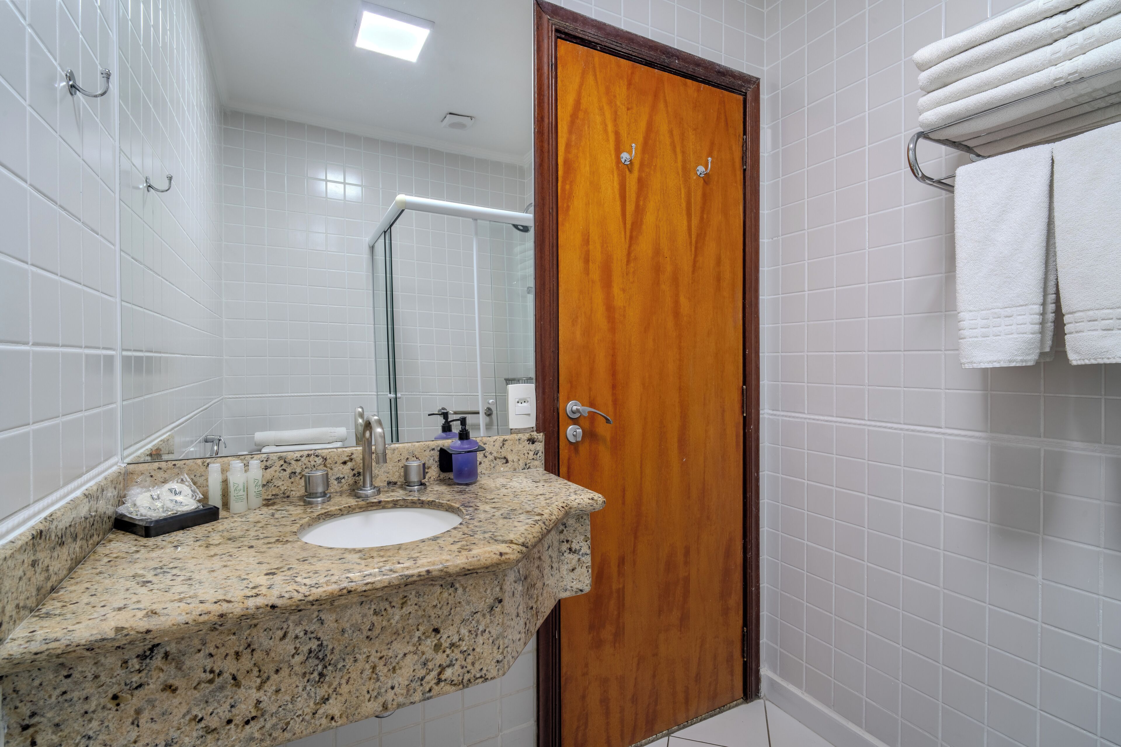 Un baño con encimera de granito, puerta de madera y paredes con azulejos blancos.