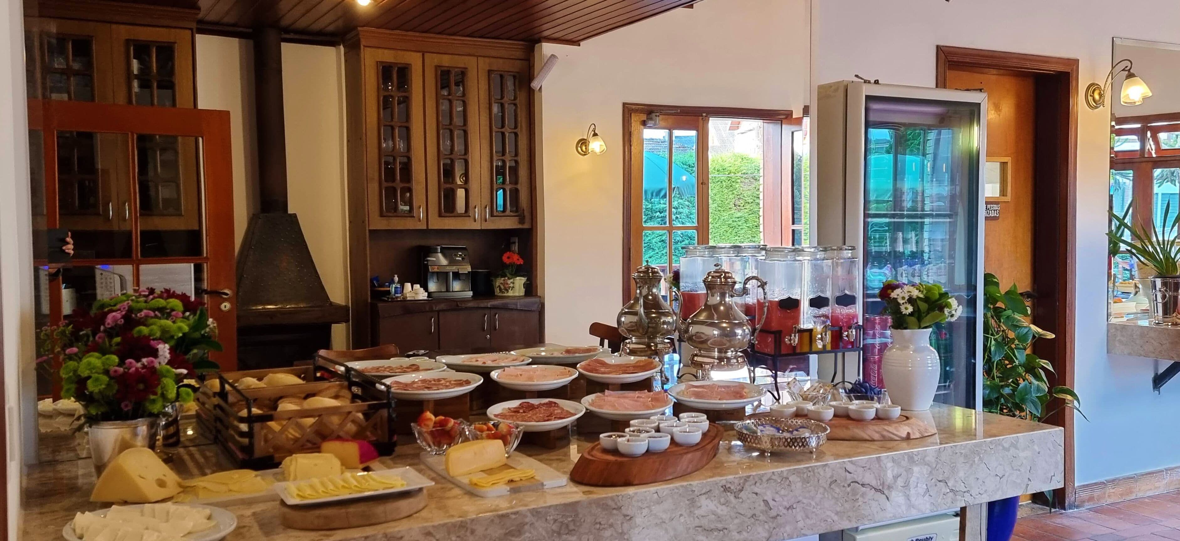 A kitchen with a marble countertop filled with various food items and utensils, wooden cabinets, and a view of greenery outside.
