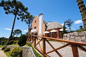 Un edificio con fachada de ladrillo, una chimenea blanca y un muro de piedra. Un puente de madera lleva a un patio con sombrillas.