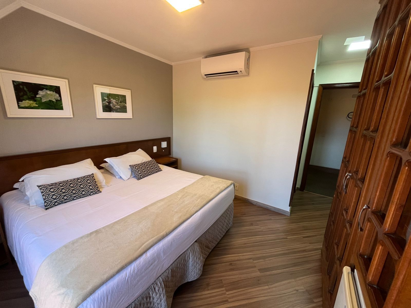 Een hotelkamer met een bed, een houten kledingkast en twee ingelijste foto's aan de muur.