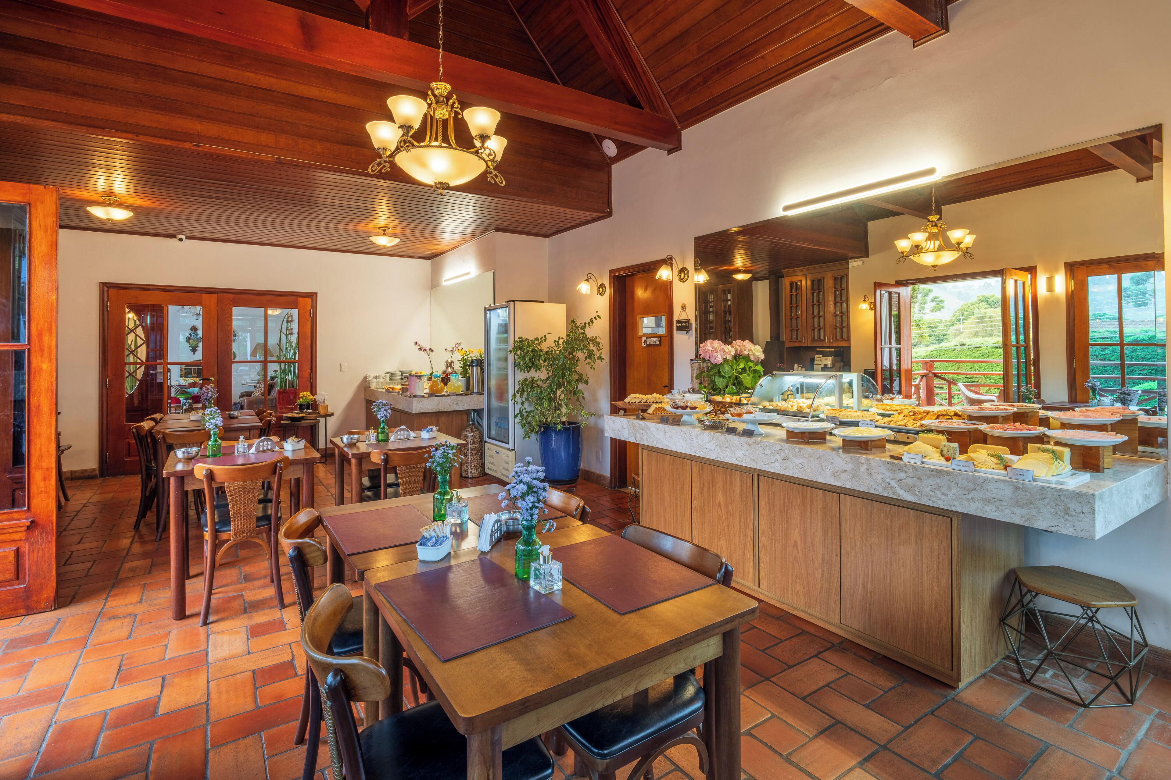 Une cuisine spacieuse dotée d’un îlot en marbre, de poutres apparentes en bois au plafond et d’un coin repas avec des tables et des chaises en bois.