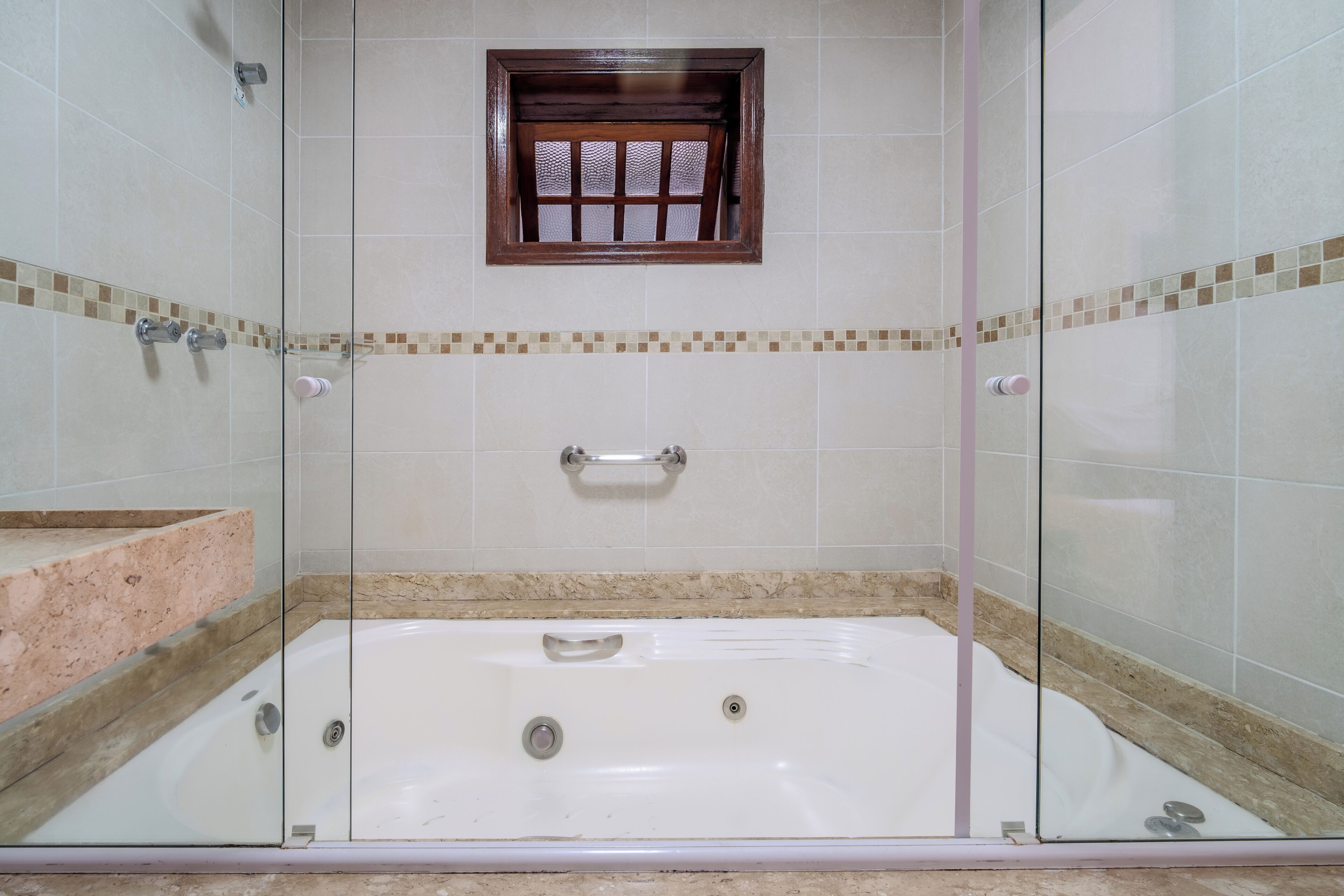 A glass-enclosed walk-in shower with a built-in window, a bathtub, and a tiled floor.