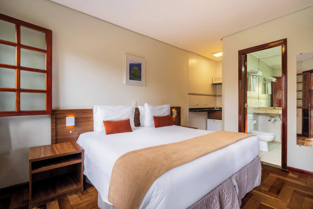 Een hotelkamer met een groot bed, een houten hoofdbord, nachtkastje, en een badkamer die door een open deur zichtbaar is.